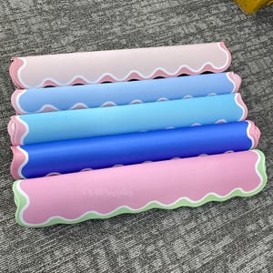 May include: Five rolled-up, colorful mats in shades of pink, blue, and green. Each mat has a wavy edge design with white trim. The text "TS Art Supplies" is visible on the bottom mat.