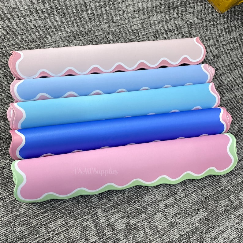 May include: Five rolled-up, colorful mats in shades of pink, blue, and green. Each mat has a wavy edge design with white trim. The text "TS Art Supplies" is visible on the bottom mat.