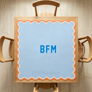 Könnte beinhalten: Eine quadratische hellblaue Matte mit einem gewellten orangefarbenen Rand und einer weißen Umrandung. Die Buchstaben BFM sind in Blau in der Mitte aufgedruckt. Der Text TS Art Supplies ist in einer hellen Schrift am unteren Rand sichtbar.
