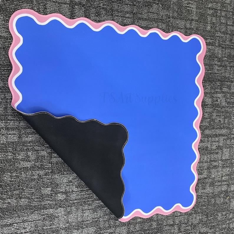 May include: A blue mat with a scalloped edge, bordered by pink and white. The underside is black. The text "TS Ad Supplies" is visible on the mat. The mat is on a gray surface.