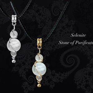 May include: Two selenite crystal pendants on black cords. The pendants are wrapped in silver and gold wire. The text "Selenite Stone of Purification" is visible in the image.