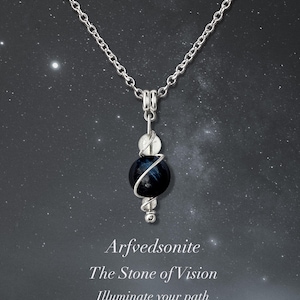 Könnte beinhalten: Eine silberne Kettenkette mit einem Anhänger aus einem blauen Arfvedsonit-Edelstein, der in Silberdraht gewickelt ist und mit zwei weißen Perlen verziert ist. Der Text "Arfvedsonit: Der Stein der Vision. Erleuchte deinen Weg." ist unter dem Anhänger dargestellt.