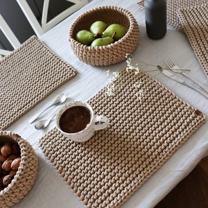 Peut inclure: Une table joliment dressée avec des sets de table en crochet beige, un panier de poires vertes et une tasse blanche tachetée remplie de café. Des couverts et un vase sombre complètent l'ambiance chaleureuse et neutre.