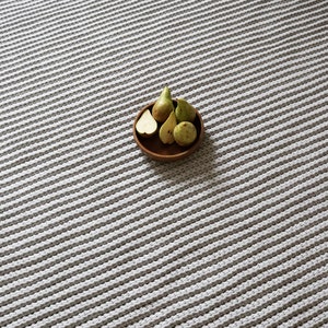 May include: A gray and white striped rug with a wooden bowl filled with pears. The bowl contains whole and sliced pears in shades of green and yellow. The rug has a textured, woven appearance.