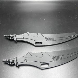 May include: Two black, futuristic-style blades with intricate designs. Each blade has a handle with a detailed mechanism and a curved, pointed blade. The blades are lying on a dark surface, suggesting a sci-fi or fantasy theme.