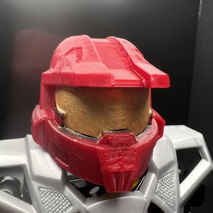 May include: A red plastic helmet with a gold visor. The helmet is designed to look like a futuristic soldier's helmet.