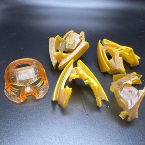 Puede incluir: Un surtido de componentes de plástico translúcidos de color naranja y amarillo, posiblemente para una estructura o modelo más grande. Las piezas están dispuestas sobre una superficie oscura, mostrando sus intrincadas formas y detalles.