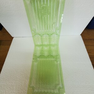 May include: A translucent, light green plastic container, possibly for holding small items. The container is rectangular with a flared top and bottom, and features vertical ridges and circular compartments. The container is open and folded in the middle.
