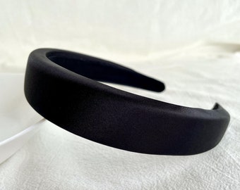 May include: A black satin headband for women. The headband is wide and has a smooth, polished finish.