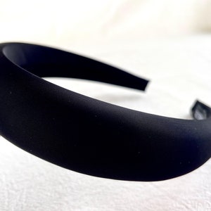 K&ouml;nnte beinhalten: Ein schwarzes Stirnband aus weichem, glattem Stoff. Das Stirnband ist breit und hat ein schlichtes, klassisches Design.
