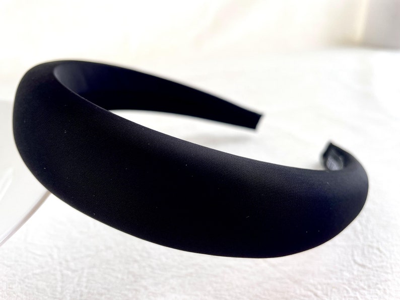 K&ouml;nnte beinhalten: Ein schwarzes Stirnband aus weichem, glattem Stoff. Das Stirnband ist breit und hat ein schlichtes, klassisches Design.