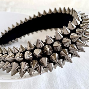 May include: A silver headband with a row of pointy metal spikes. The headband is made of a black fabric base.