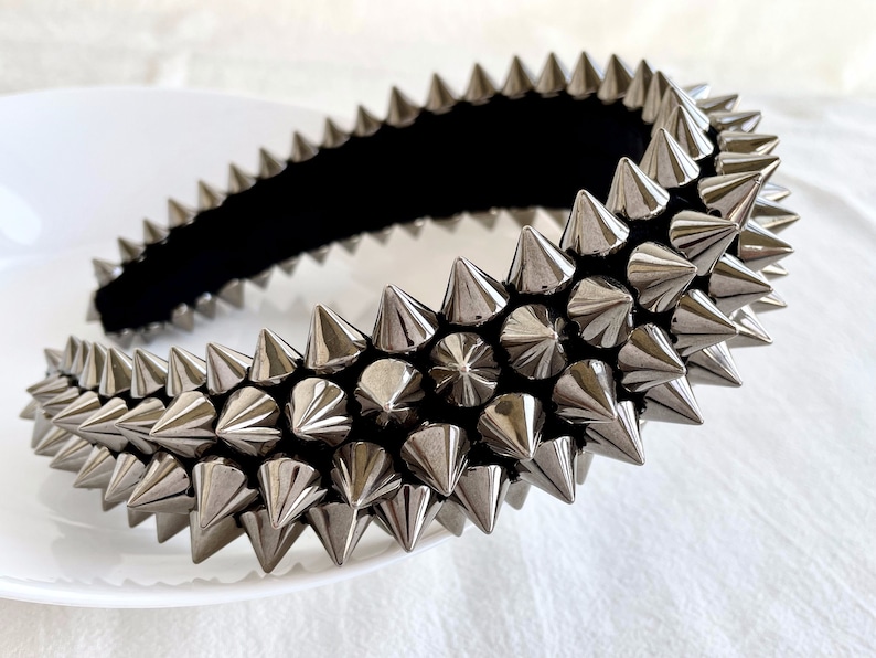 May include: A silver headband with a row of pointy metal spikes. The headband is made of a black fabric base.