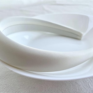 K&ouml;nnte beinhalten: Ein wei&szlig;es Satin-Haarband, ein dickes, breites Haarband f&uuml;r Haare, auf einem wei&szlig;en Teller.