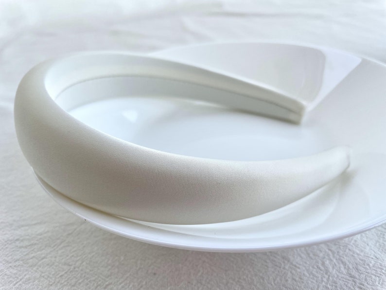 K&ouml;nnte beinhalten: Ein wei&szlig;es Satin-Haarband, ein dickes, breites Haarband f&uuml;r Haare, auf einem wei&szlig;en Teller.