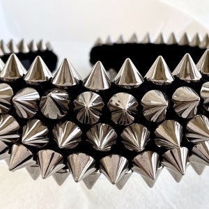 May include: A black headband with silver pyramid-shaped studs. The headband is covered in rows of studs, creating a punk rock aesthetic.