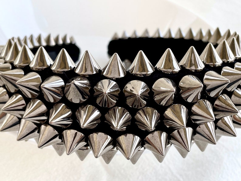 May include: A black headband with silver pyramid-shaped studs. The headband is covered in rows of studs, creating a punk rock aesthetic.