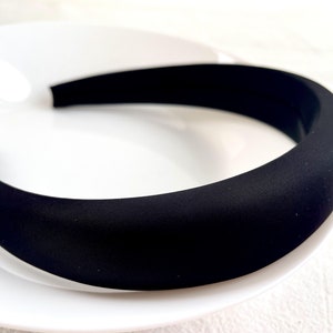 K&ouml;nnte beinhalten: Ein schwarzes gepolstertes Haarband. Das Haarband ist dick und breit und hat eine glatte, matte Oberfl&auml;che.