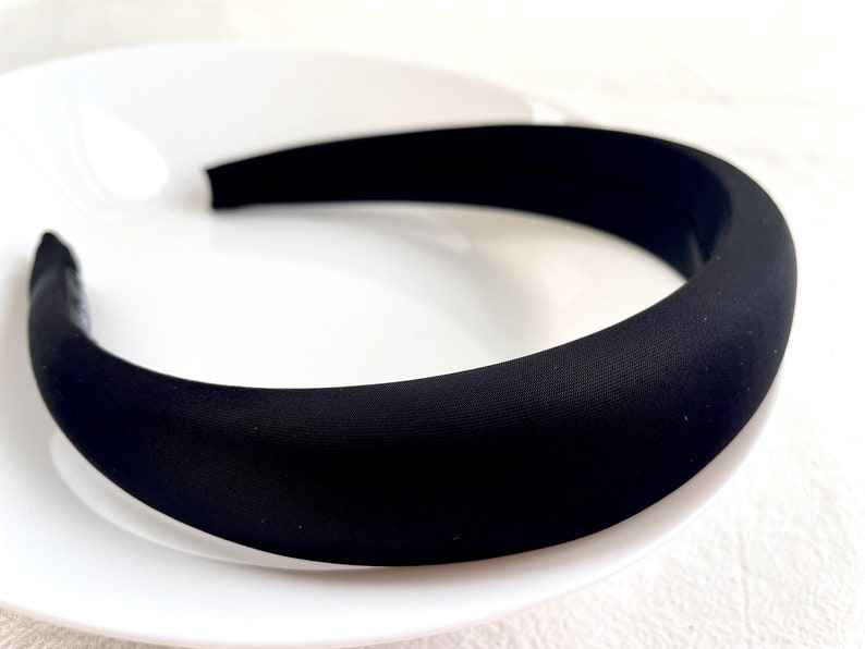 K&ouml;nnte beinhalten: Ein schwarzes gepolstertes Haarband. Das Haarband ist dick und breit und hat eine glatte, matte Oberfl&auml;che.