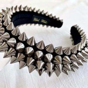 May include: A silver headband with a row of pointy metal spikes. The headband is made of black velvet and has the text "Hand Made" on the back.