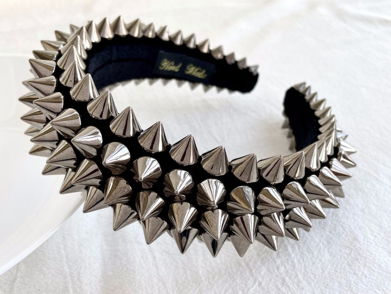 May include: A silver headband with a row of pointy metal spikes. The headband is made of black velvet and has the text "Hand Made" on the back.