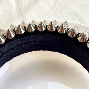 May include: A black headband with silver metal spikes. The headband is made of a soft, stretchy material and is designed to fit comfortably on the head.