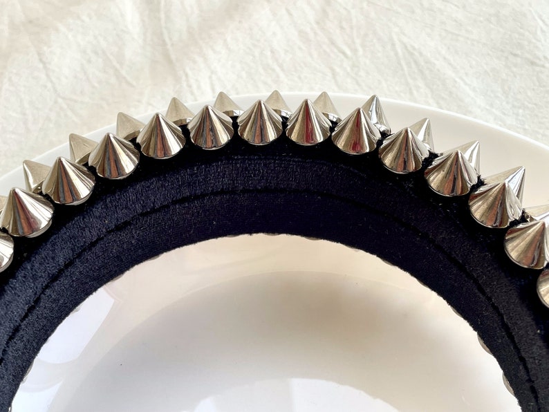 May include: A black headband with silver metal spikes. The headband is made of a soft, stretchy material and is designed to fit comfortably on the head.