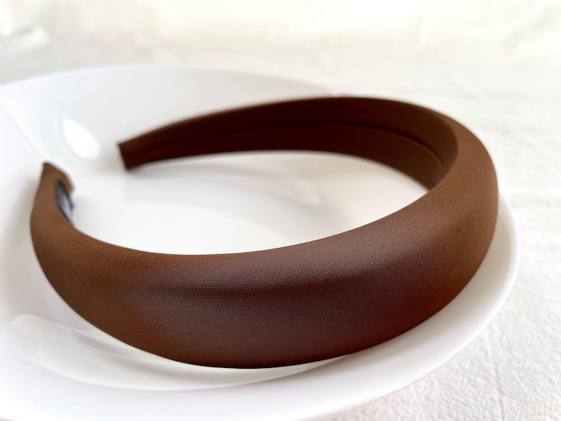 K&ouml;nnte beinhalten: Ein braunes gepolstertes Stirnband f&uuml;r Haare. Das Stirnband ist aus einem weichen, glatten Stoff.