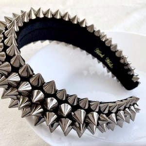 May include: A silver headband with a row of pointy spikes. The headband is made of black fabric and has the words "Hand Made" written on it.