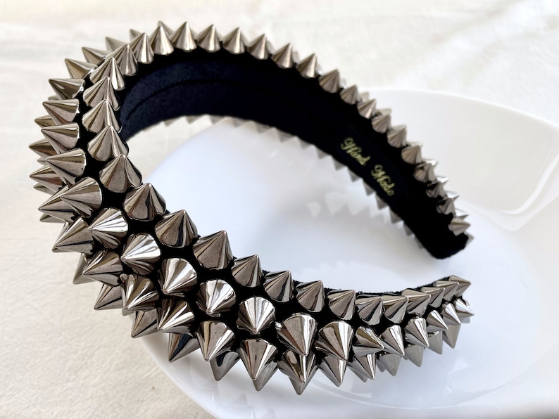 May include: A silver headband with a row of pointy spikes. The headband is made of black fabric and has the words "Hand Made" written on it.