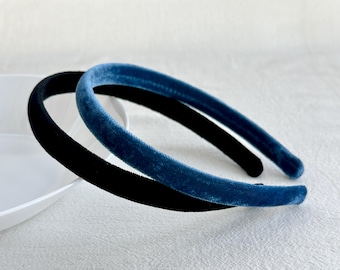 May include: Two velvet headbands, one black and one blue, are shown on a white surface. The headbands are both thin and have a simple design.