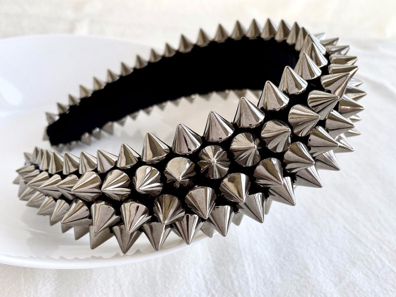 May include: A silver headband with a row of sharp, pointed spikes. The headband is made of a black fabric base and is covered in silver spikes.