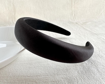 May include: A black padded headband for hair. The headband is made of a soft, smooth fabric.