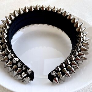 May include: A black headband with silver metal spikes. The headband is on a white plate.