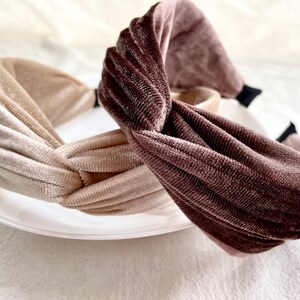 以下が含まれることがあります： ねじれた結び目のデザインのベルベット製のヘッドバンドが2本。1本は茶色、もう1本はベージュです。