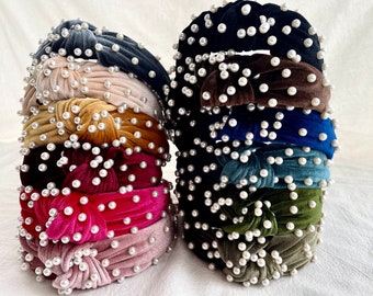 May include: A stack of eight velvet headbands with pearl embellishments. The headbands are in various colors, including black, brown, blue, teal, green, pink, and beige.