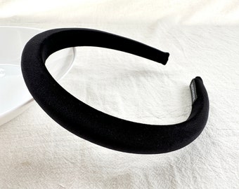 Könnte beinhalten: Ein schwarzes, gepolstertes Haarband mit weicher, samtiger Textur. Das Haarband ist ein breiter Stil, der bequem auf dem Kopf sitzt. Das Accessoire ist einfarbig schwarz und eignet sich für verschiedene Frisuren und Anlässe.