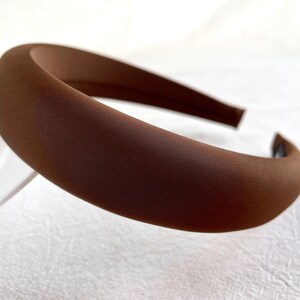 K&ouml;nnte beinhalten: Ein braunes gepolstertes Stirnband f&uuml;r Haare. Das Stirnband ist aus einem weichen, glatten Stoff.