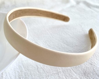 May include: A wide, off-white headband made of faux leather. The headband is smooth and has a slight sheen.