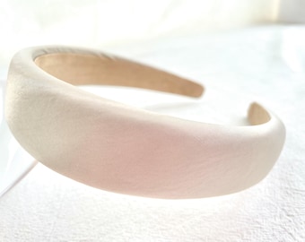 Könnte beinhalten: Ein breites, cremefarbenes Satin-Haarband. Das Haarband ist glatt und hat einen leichten Glanz.
