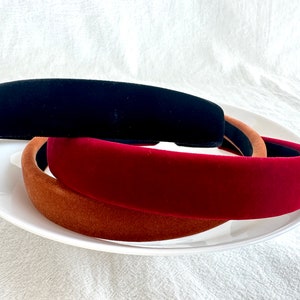 May include: Three velvet headbands in black, burgundy, and brown. The headbands are stacked on top of each other on a white plate.