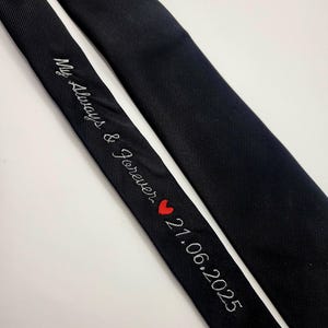 May include: Two black ties are shown against a white backdrop. One tie features the embroidered text "My Always & Forever" with a red heart and the date "21.06.2025". The other tie is plain black.