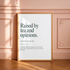May include: A framed vertical wall art print featuring the dark green text Raised by tea and opinions, followed by Persian script, a phonetic pronunciation guide, and a descriptive paragraph about a Persian childhood essential in a light wood frame.