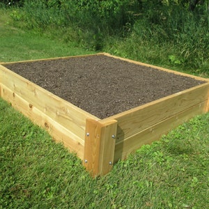 May include: A raised garden bed made of natural wood planks. The bed is filled with dark brown soil and is sitting on a green grassy lawn.