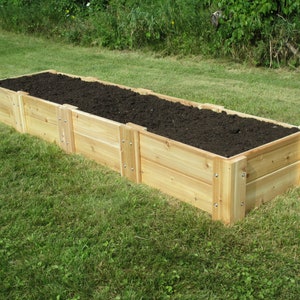 May include: A raised garden bed made of untreated cedar wood. The bed is filled with dark brown soil and is sitting on a green lawn.