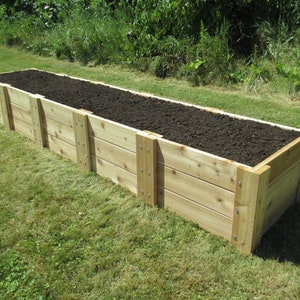 May include: A raised garden bed made of untreated cedar wood planks. The bed is filled with dark brown soil and is sitting on a green lawn.