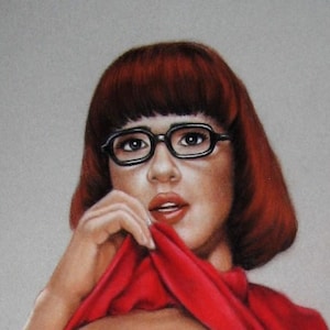 May include: A portrait of a person with short, auburn hair and black-framed glasses. The person is wearing a red top and is holding the fabric near their face. The background is a solid, light gray color.