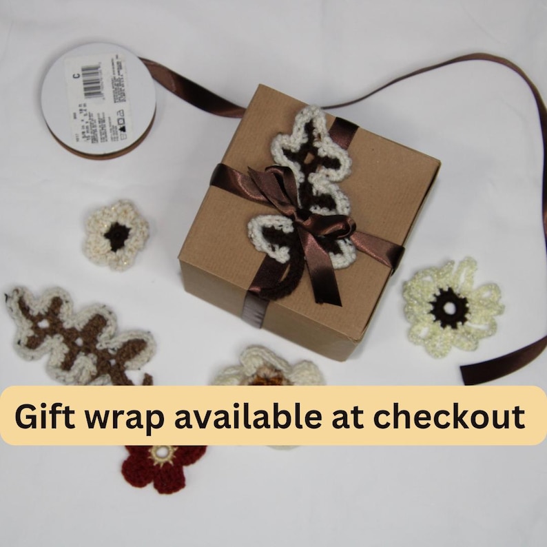 May include: A brown gift box tied with a brown ribbon, adorned with a crocheted floral embellishment. Scattered around are crocheted flowers and a spool of brown ribbon. The text "Gift wrap available at checkout" is displayed.