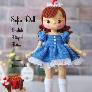 Könnte beinhalten: Eine gehäkelte Puppe, die ein blaues Kleid, weiße Socken und rote Schuhe trägt. Die Puppe hat braunes Haar, eine rote Weihnachtsmütze und eine weiße Spitzenborte an ihrem Kleid. Die Puppe steht auf einer weißen Oberfläche mit einem kleinen gehäkelten Rentier, das eine Geschenkbox hält.