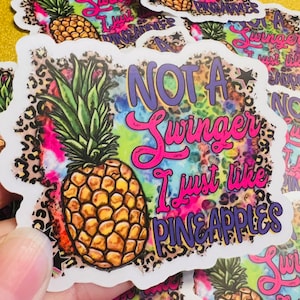 May include: A white sticker with a colorful tie-dye background and a black leopard print. The sticker features a pineapple and the text "Not a Swinger I just like Pineapples".